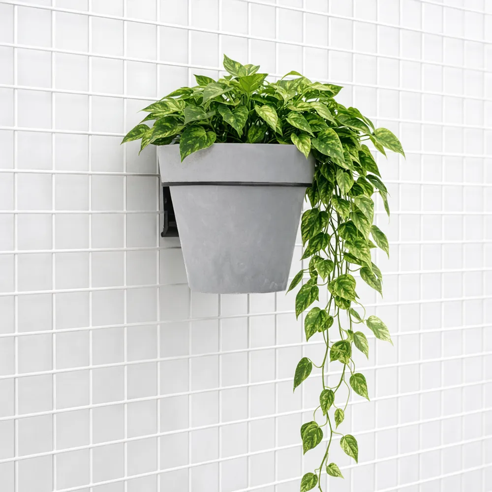 Blumentopf mit gr&uuml;ner Pflanze, aufgeh&auml;ngt an einem schwarzen Loft-Gitter mit einem Blumentopfhalter.