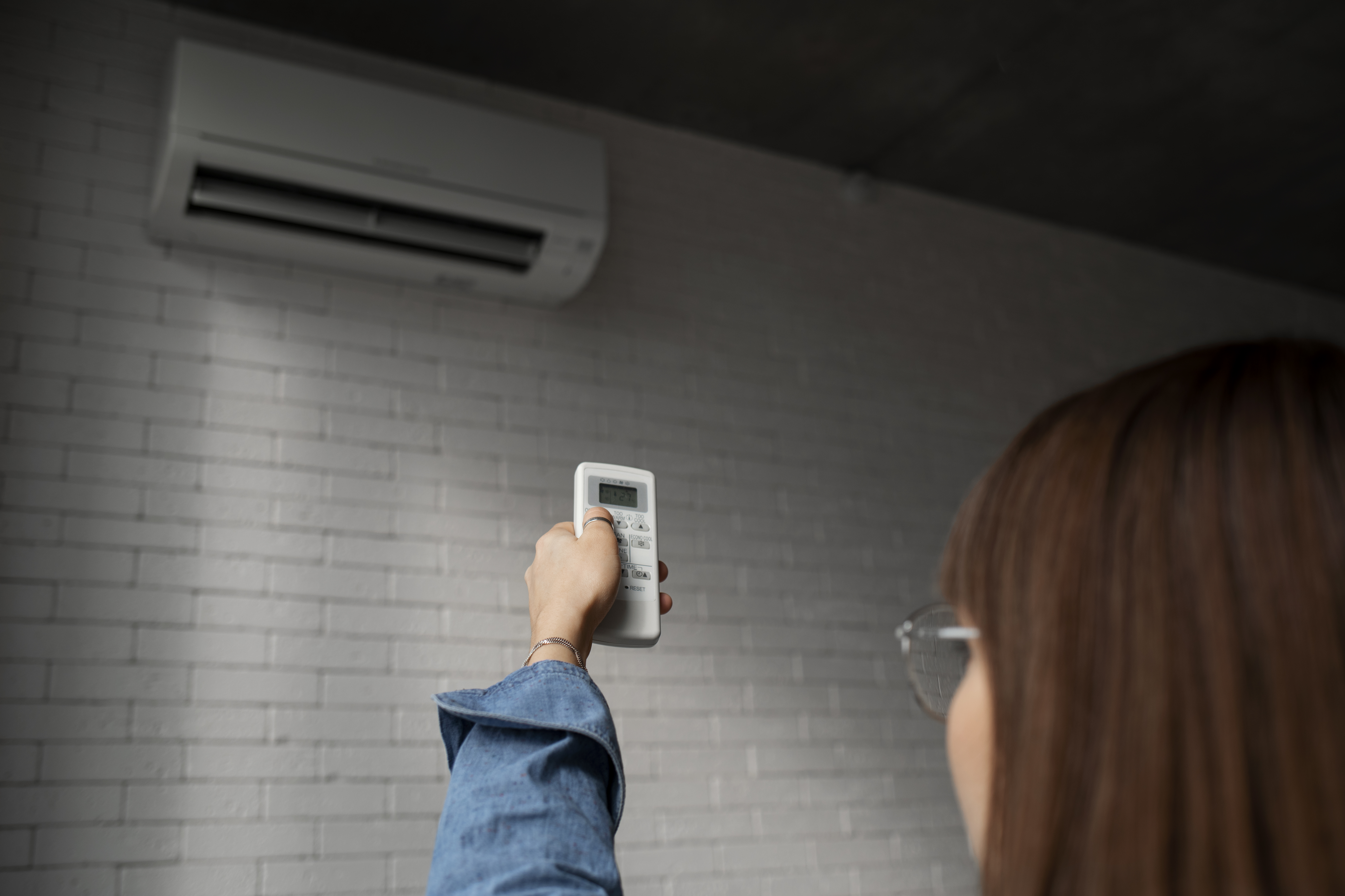 Frau bedient Klimaanlage mit Fernbedienung &ndash; richtige L&uuml;ftung und Wartung zur Reduzierung von W&auml;rmeverlusten und Heizkosten
