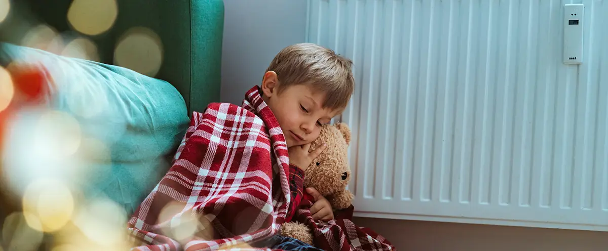 Kind sitzt eingekuschelt neben einem Heizk&ouml;rper &ndash; Symbolbild f&uuml;r W&auml;rmeverlust und effizientes Heizen im Haushalt