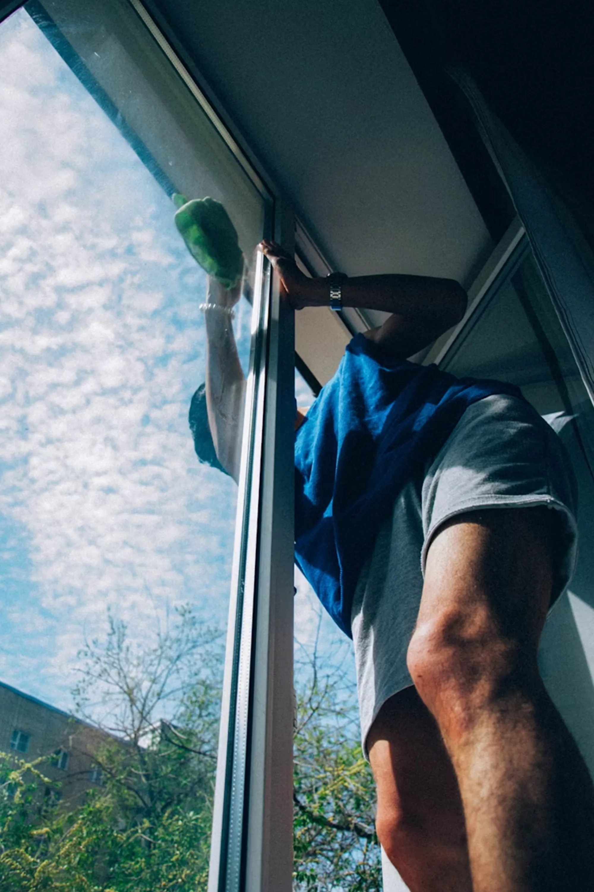 Person reinigt eine Fensterscheibe von au&szlig;en mit einem Schwamm an einem ge&ouml;ffneten Fenster.