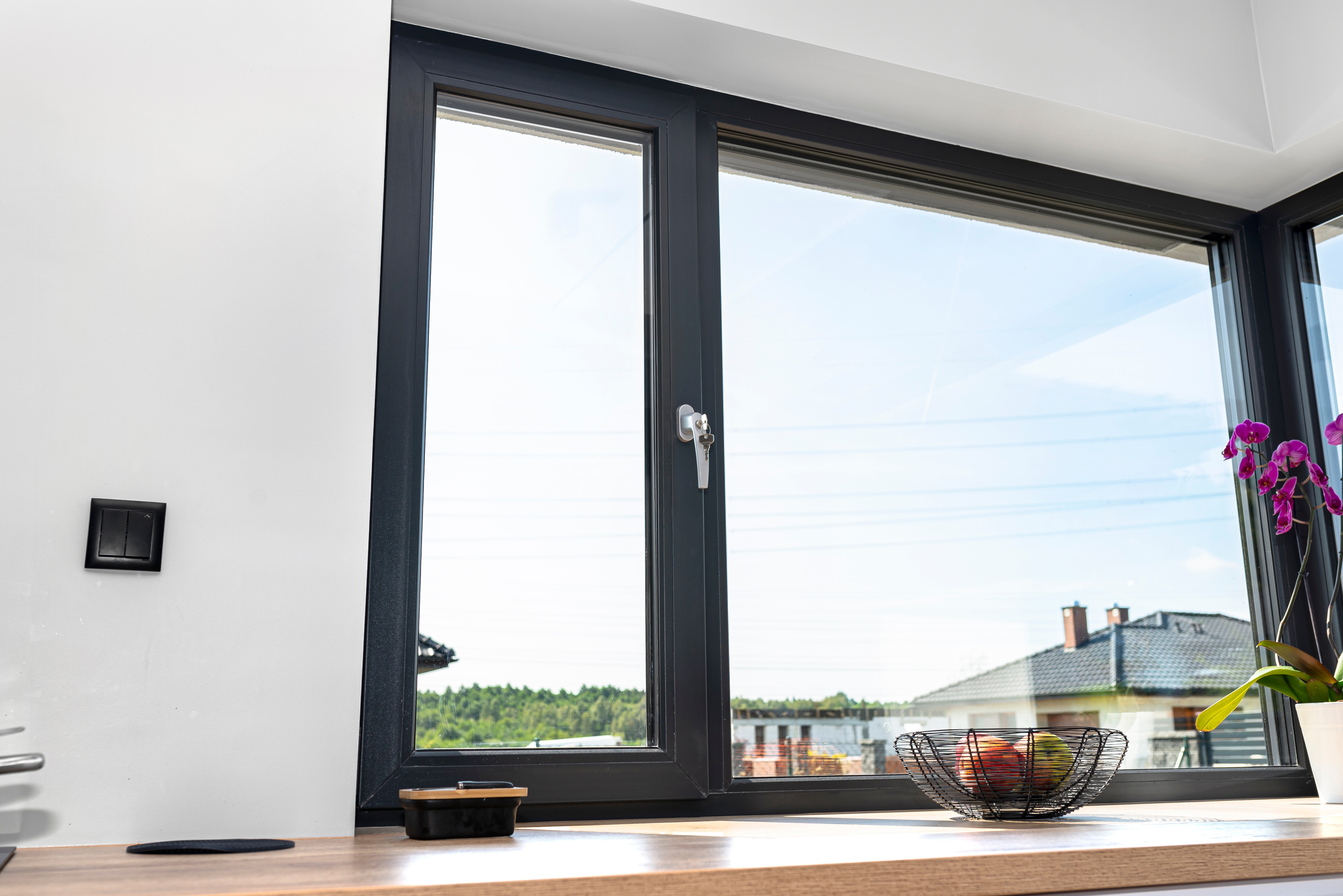 Gro&szlig;es modernes Fenster mit schwarzem Rahmen und Fensterbank mit Dekoration im Wohnraum.