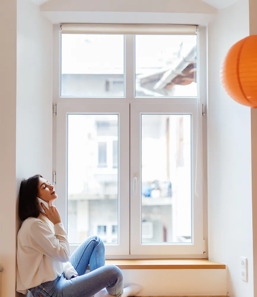 Person sitzt am Fenster in einem hellen Raum – Beispiel für Wärmeverluste bei Zweifachverglasung.